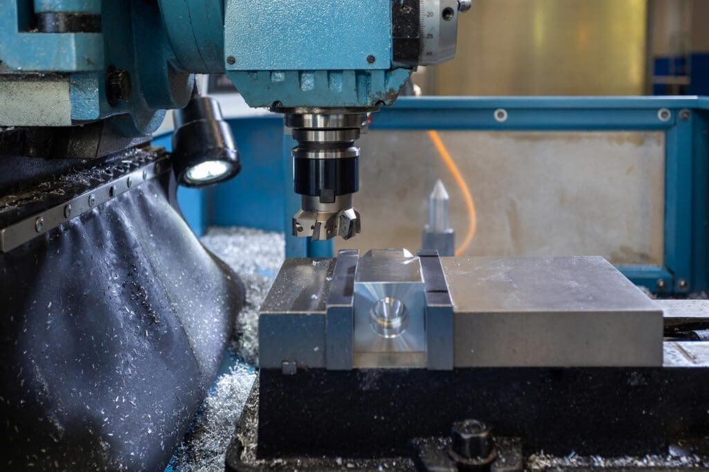A close-up of a blue CNC milling machine in operation, focusing on the spindle and cutting tool